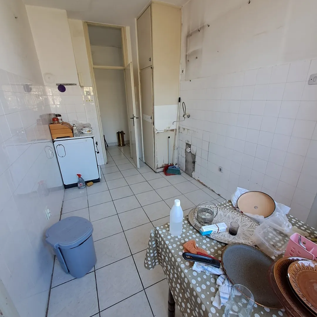 Starija i neuređena kuhinja sa trpezarijskim stolom i vidljivim znacima dotrajalosti.