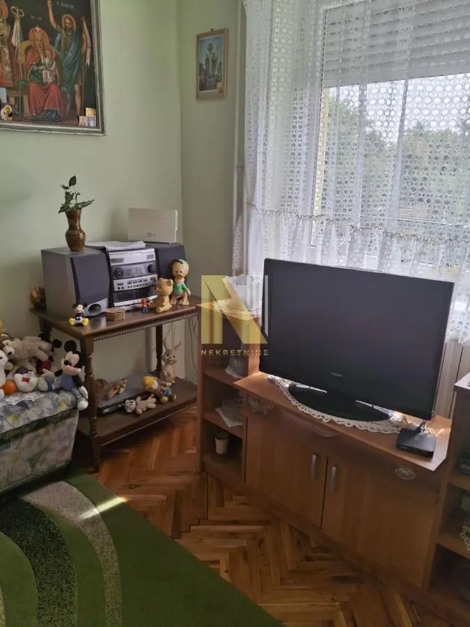 Dnevna soba sa drvenim podom, televizorom i komodom.