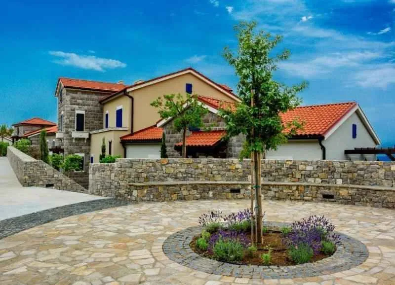 Pogled na eksterijer zgrade sa uređenim dvorištem i kamenom popločanim platoom.