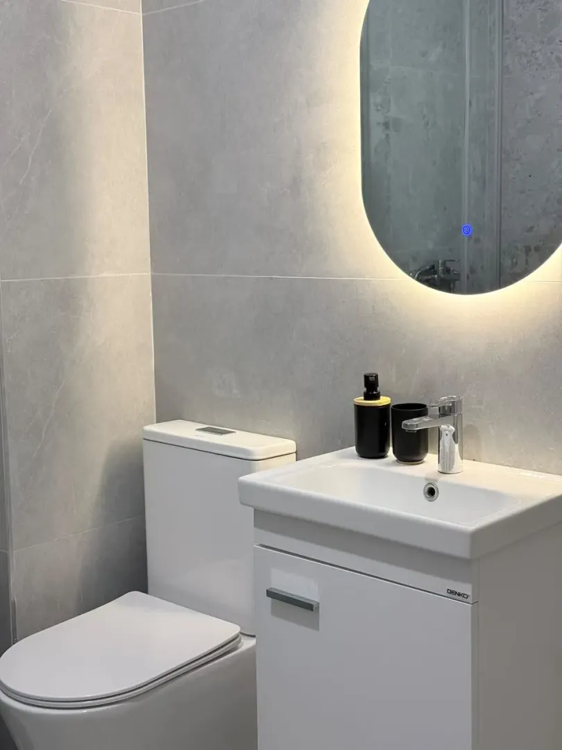 Modern bathroom with a sink, toilet, and illuminated mirror.