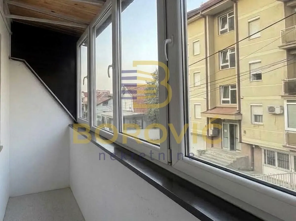 Zastakljeni balkon sa pogledom na susednu zgradu i ulicu.