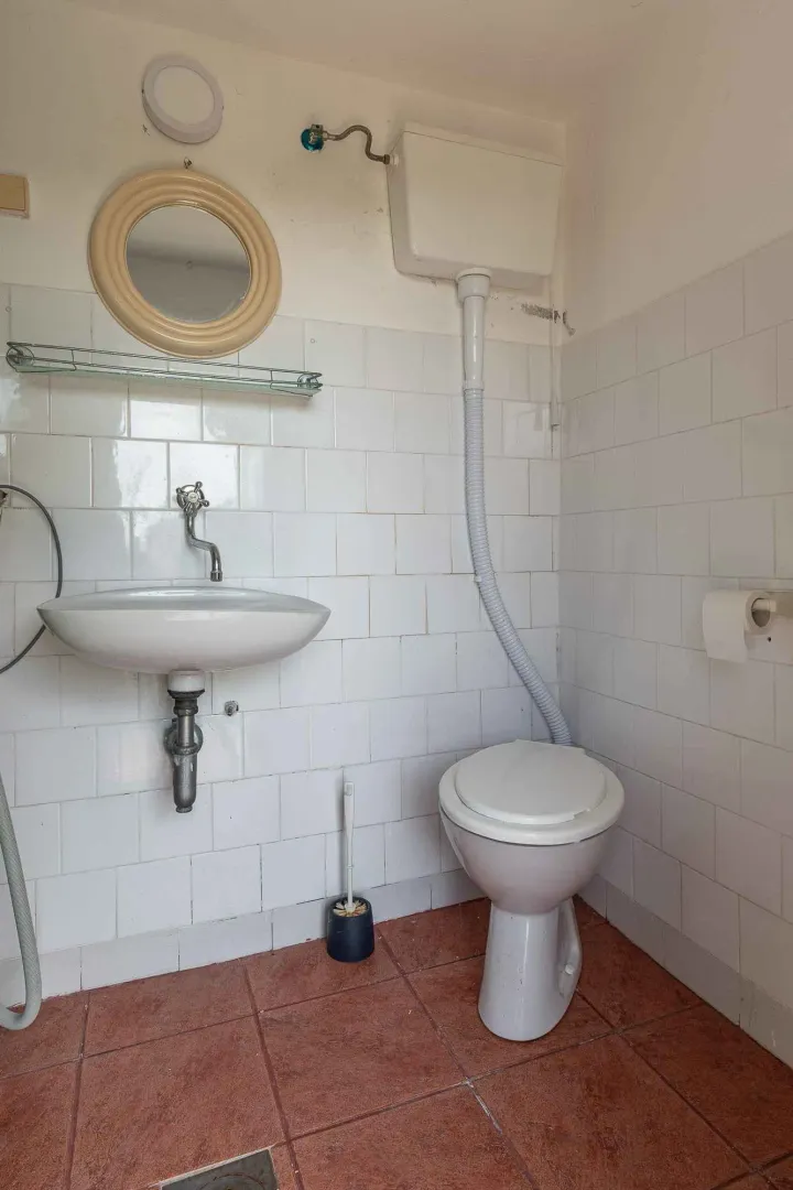 Manje kupatilo sa bijelim pločicama, umivaonikom i wc šoljom.