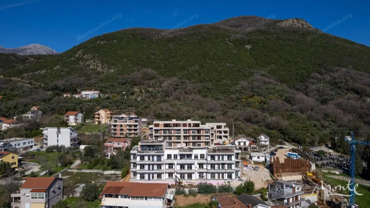 Pogled iz vazduha na stambeni objekat u izgradnji okružen zelenilom i brdima.