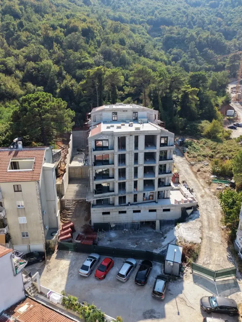 Pogled iz vazduha na stambenu zgradu u izgradnji okruženu zelenilom.
