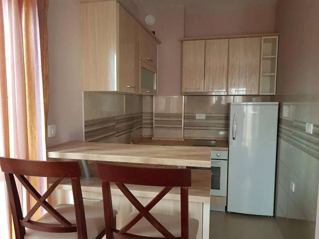 Small kitchen with wooden units, a breakfast bar and a refrigerator.