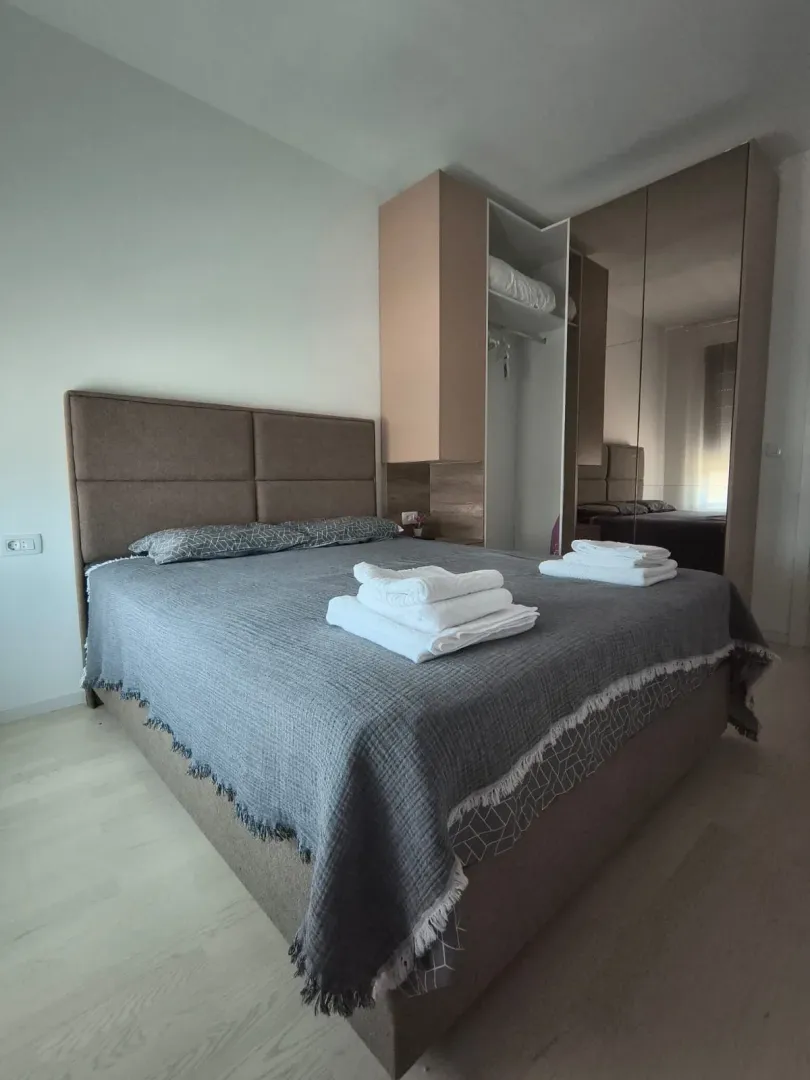 Namještena spavaća soba sa bračnim krevetom i ugradnim plakarom sa ogledalom.