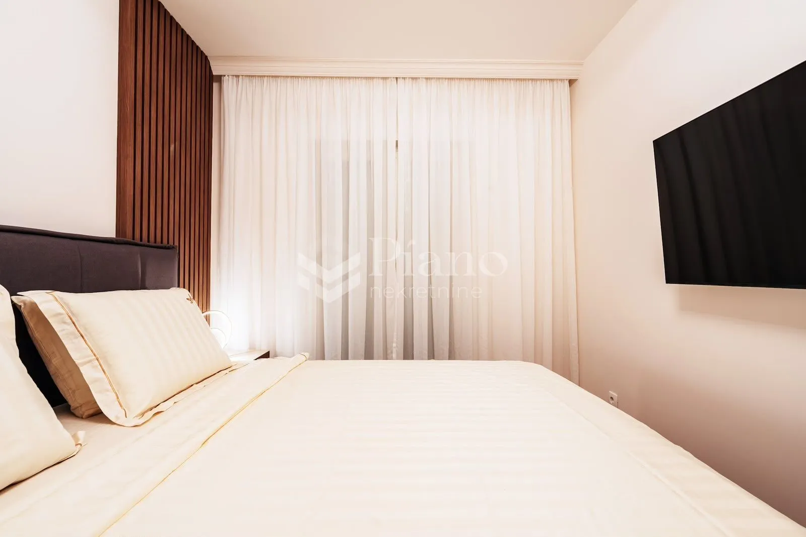 Modern bedroom with a double bed, white curtains and a wall-mounted TV.