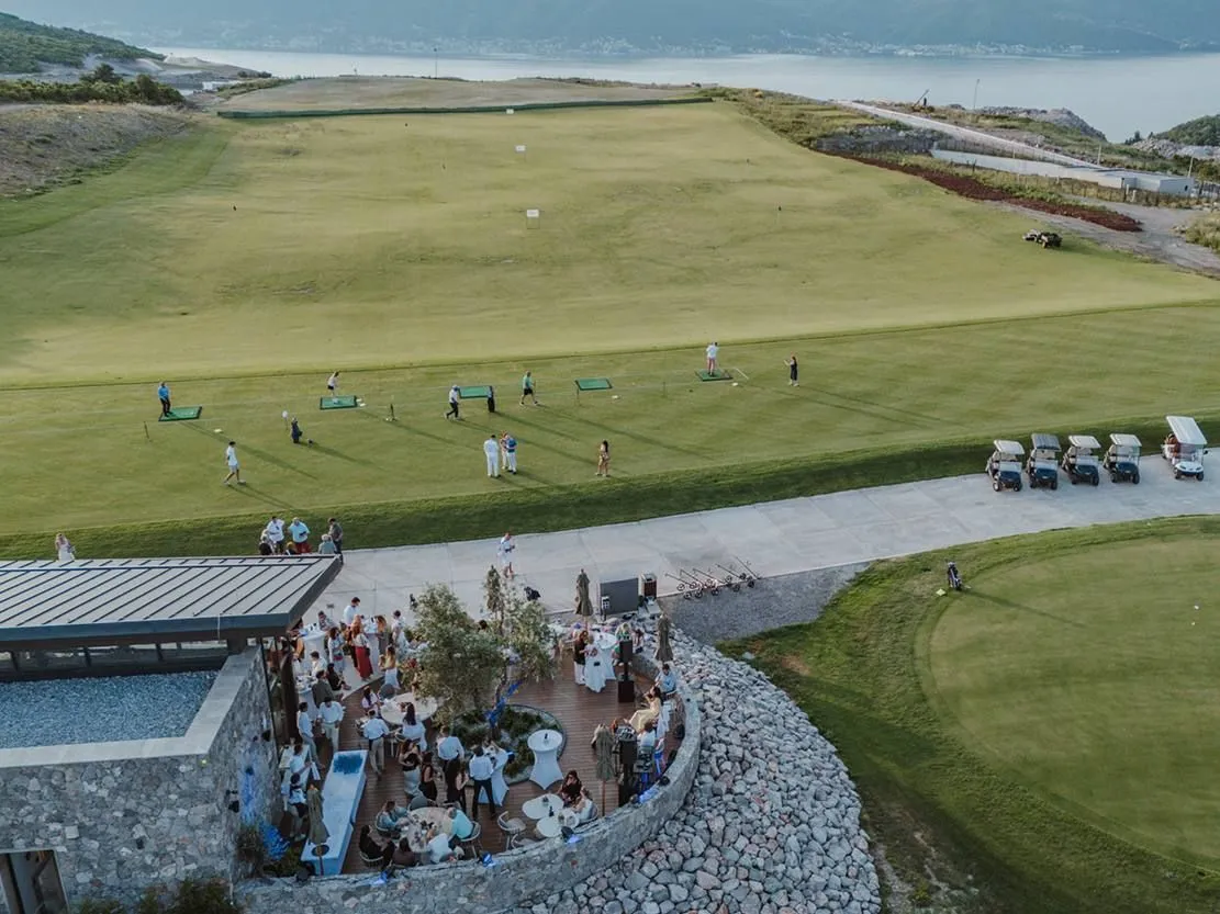 Pogled iz vazduha na spoljašnjost objekta i golf teren sa ljudima.