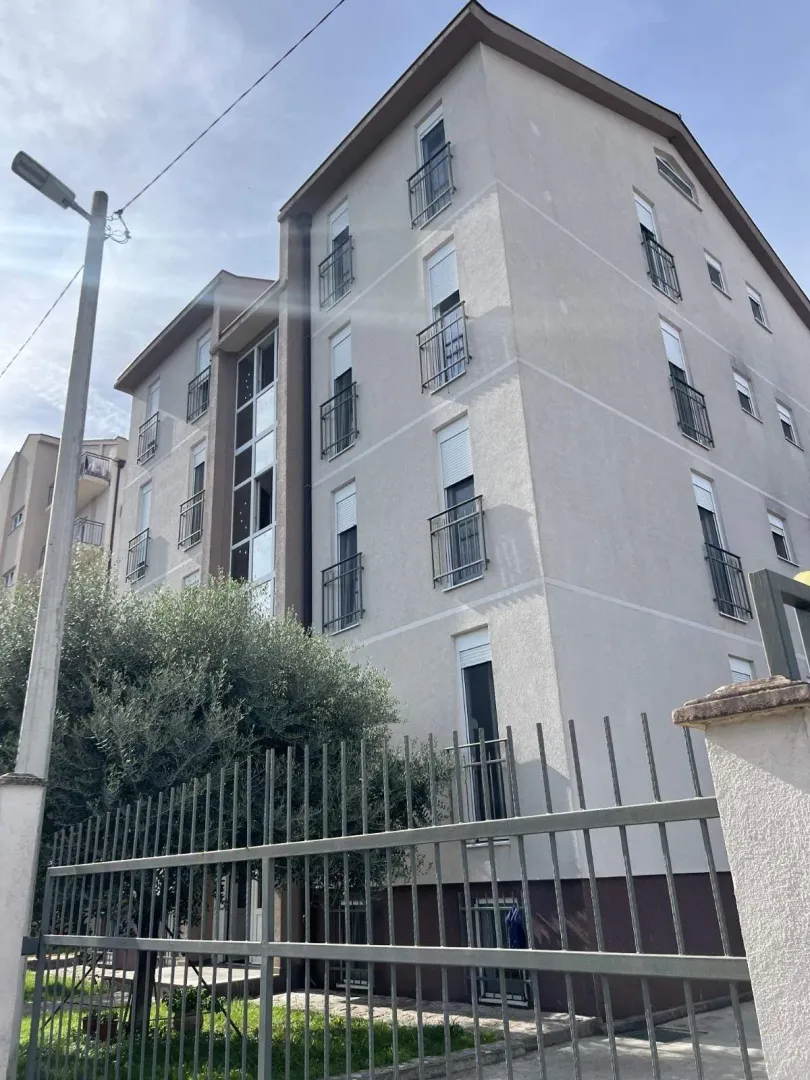 Fasada višespratne stambene zgrade sa metalnom ogradom u prvom planu.
