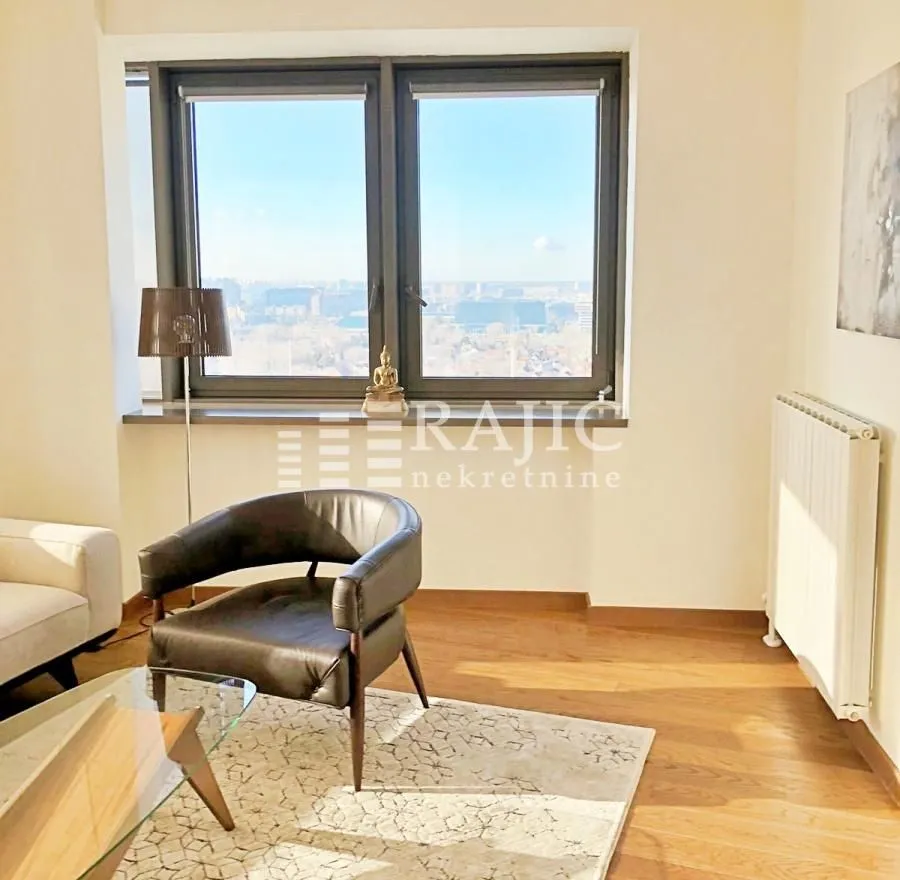 Living room with an armchair, couch, and a window overlooking the city.