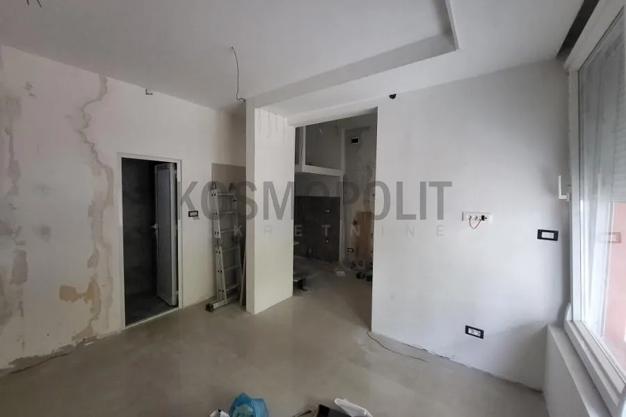 Prazna prostorija u toku renoviranja sa belim zidovima i pločicama na podu.