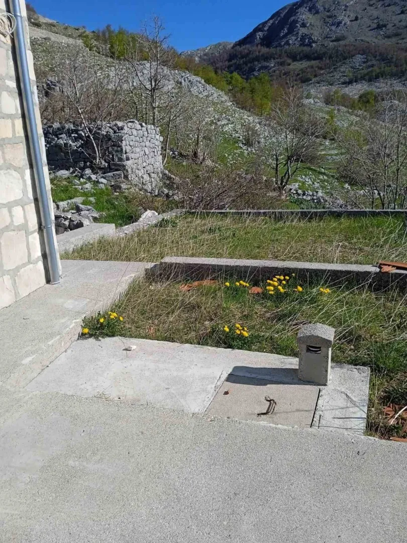 Dvorište ispred kamene kuće u planinskom okruženju.