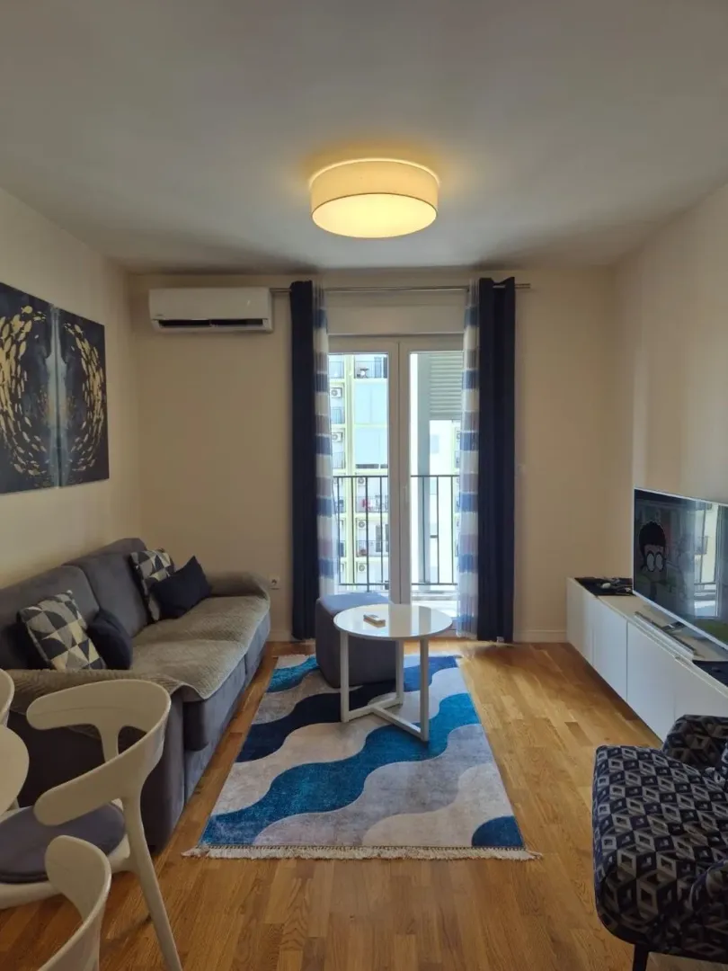 Namještena dnevna soba sa garniturom, stočićem, TV-om i izlazom na terasu.