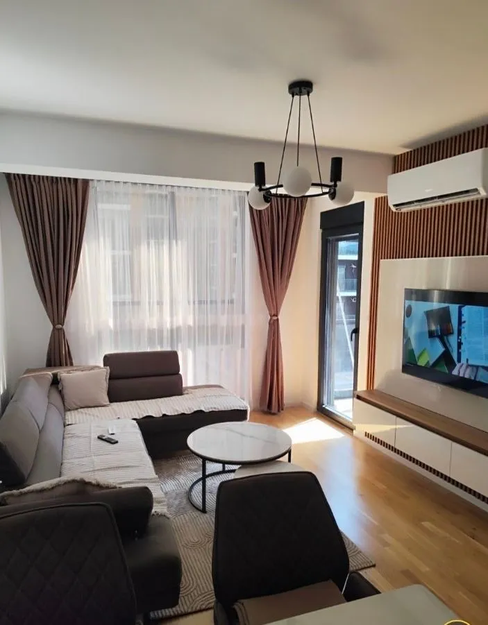 Moderan i svijetao dnevni boravak sa ugaonom garniturom i TV uređajem.