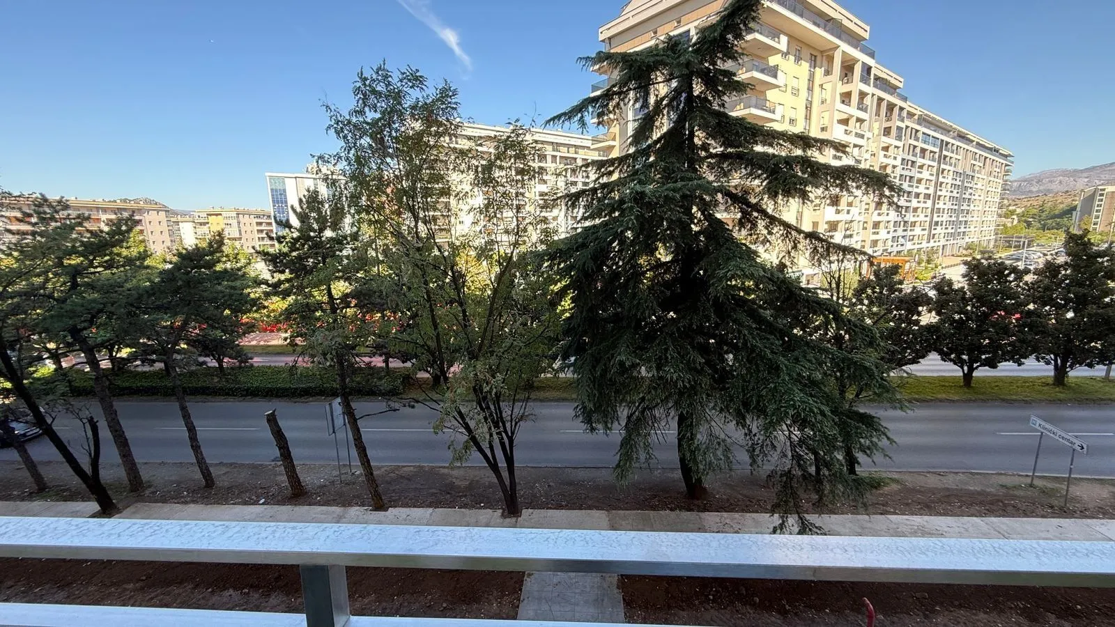View from the terrace overlooking the street, greenery, and surrounding buildings.