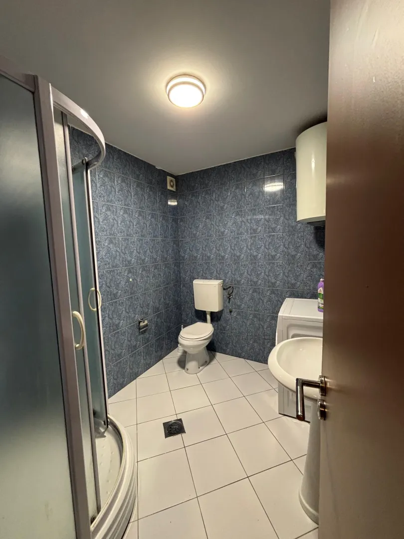 Small bathroom with a shower cabin, toilet, sink, and blue wall tiles.