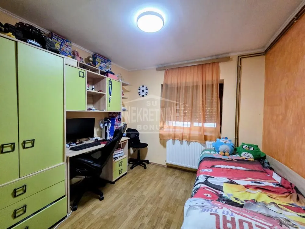 Dečja soba sa krevetom, radnim stolom i zelenim ormarima.