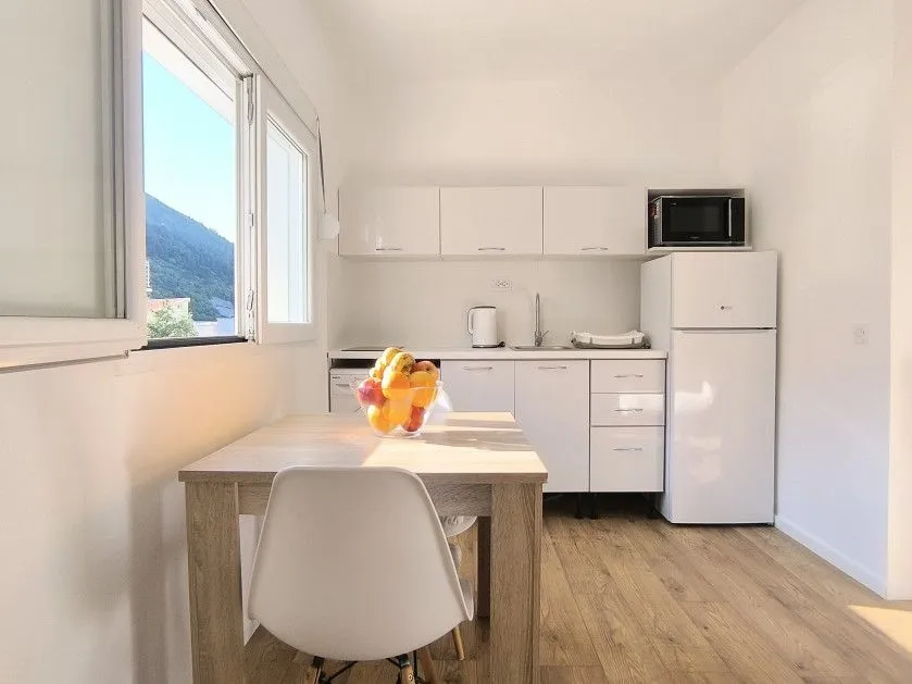 Small white kitchen with a dining table and a view through the window.