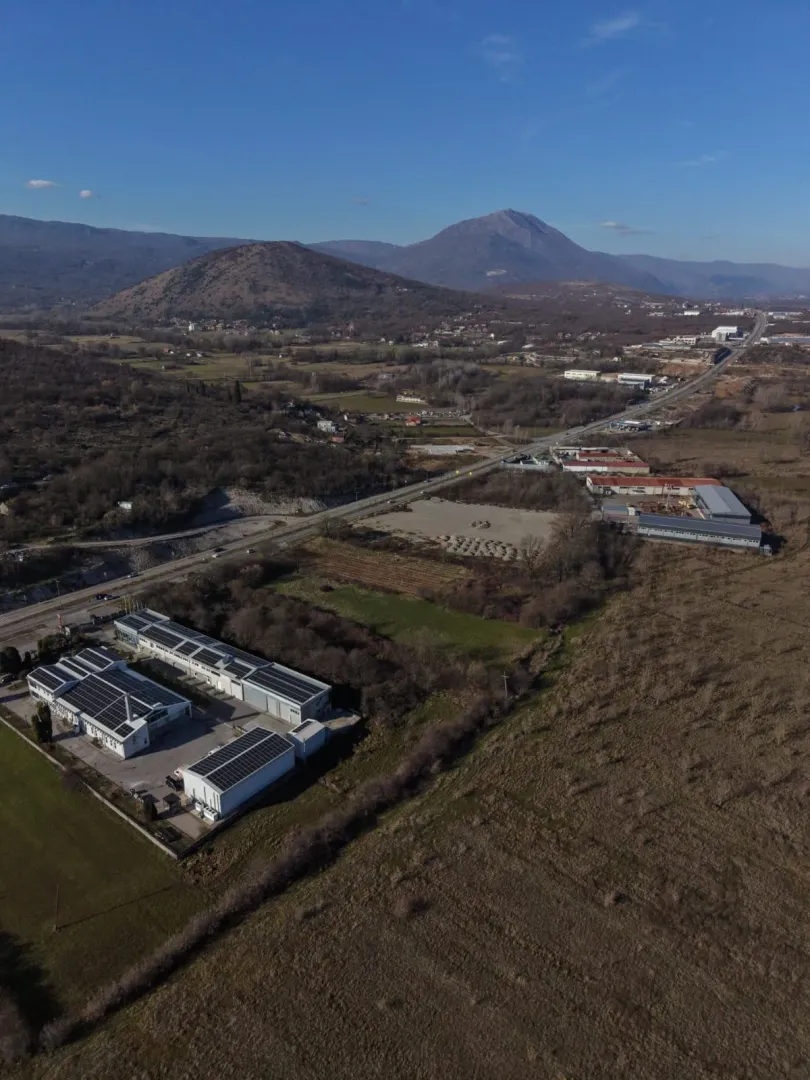 Pogled iz vazduha na industrijski objekat i okolno zemljište sa planinama u pozadini.