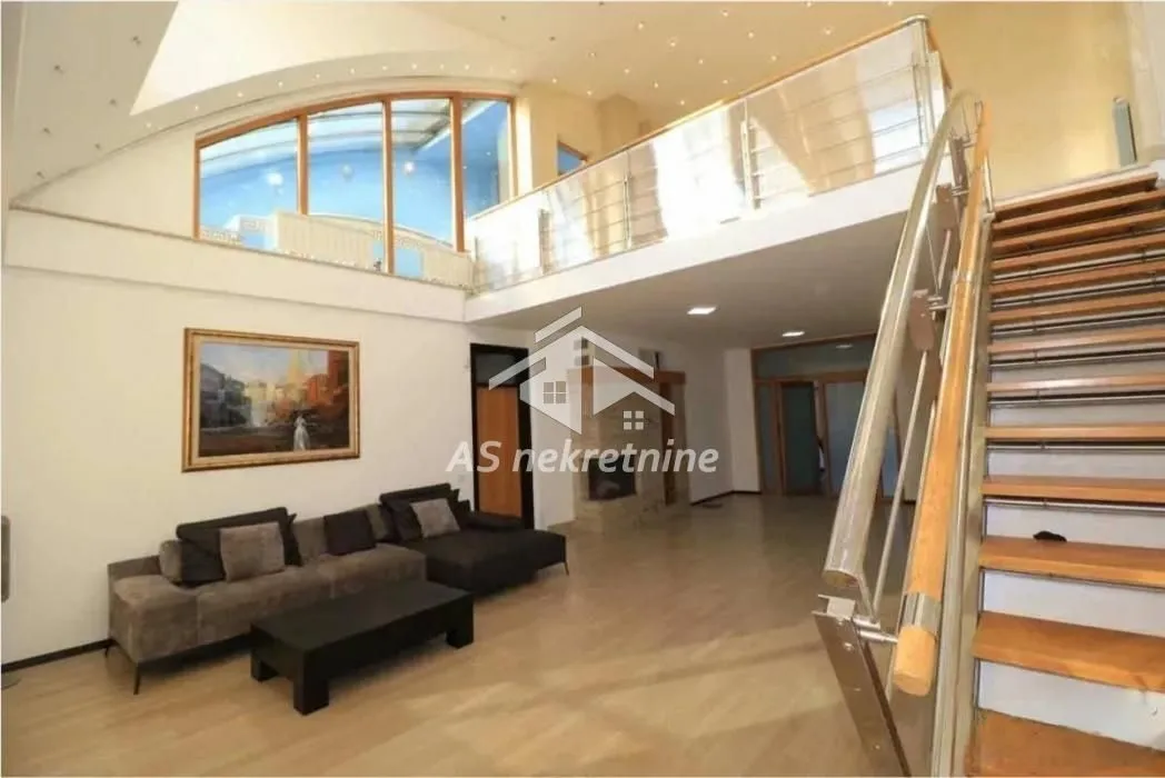 Spacious living room with high ceiling, seating set and stairs leading to the gallery.