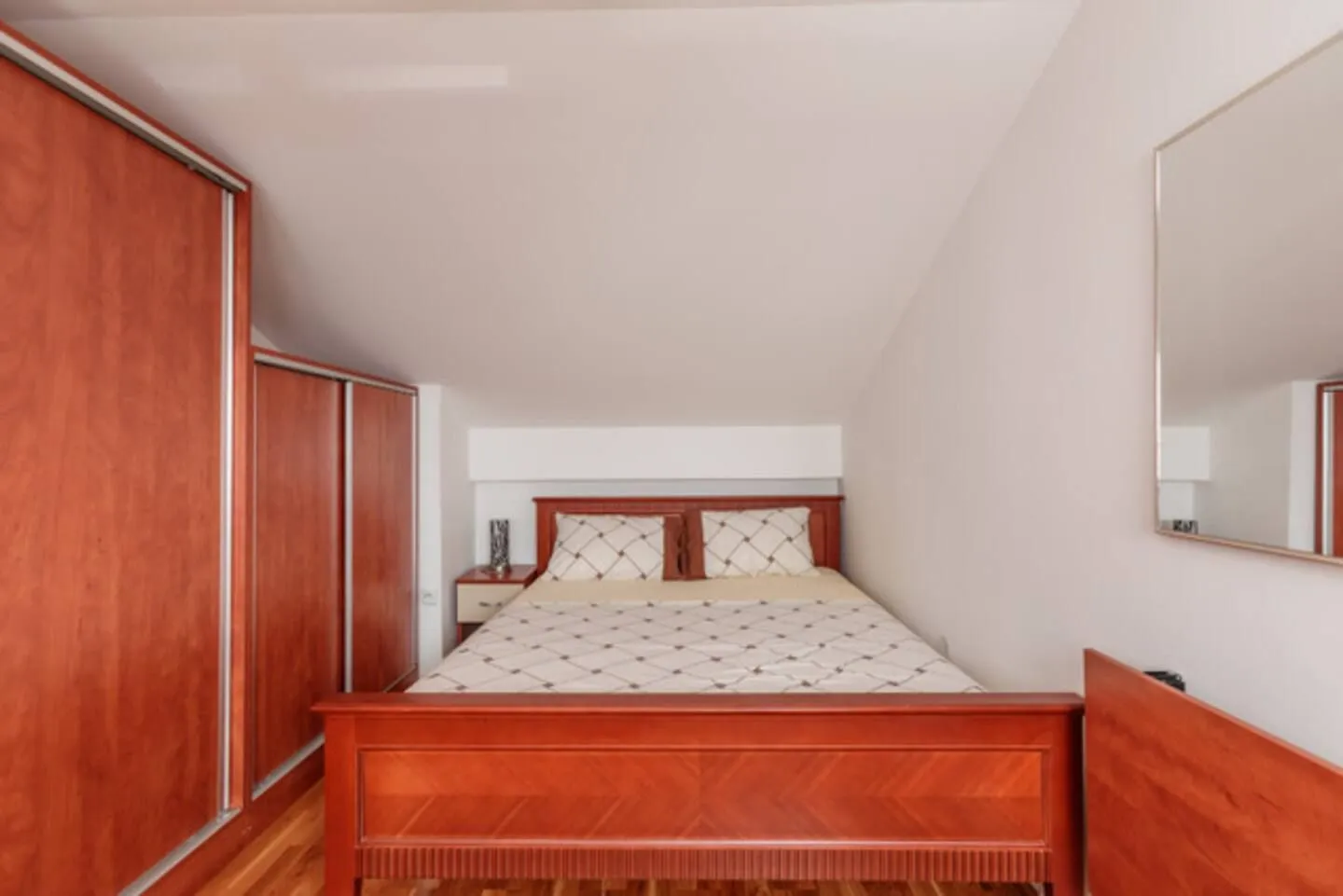 Furnished bedroom with a double bed, wooden wardrobes, and a wall mirror.