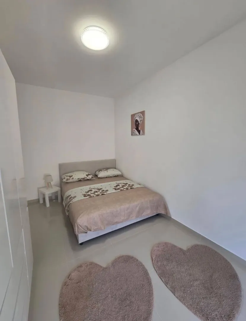Svjetla spavaća soba sa bračnim krevetom i bijelim namještajem.