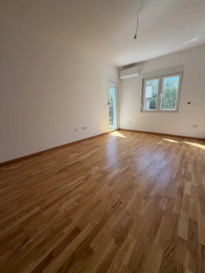 Prazna soba sa parketom, klima-uređajem i izlazom na terasu.