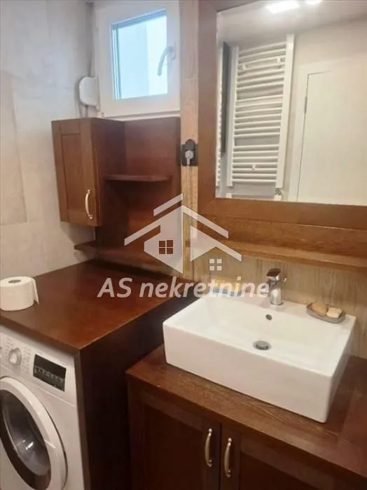 Kupatilo sa umivaonikom, drvenim elementima i veš mašinom.