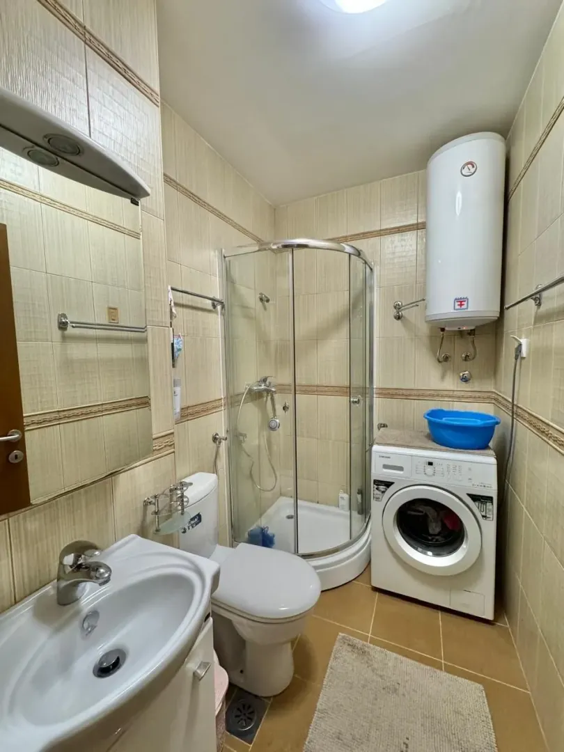 Manje kupatilo sa tuš kabinom, umivaonikom, WC šoljom i veš mašinom.