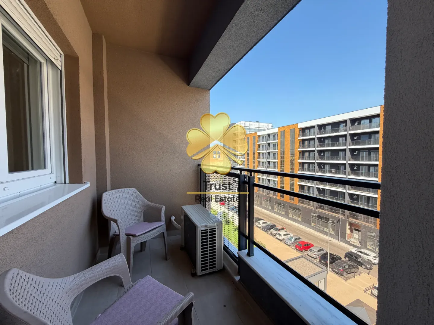 Small furnished balcony with seating set and view of buildings.