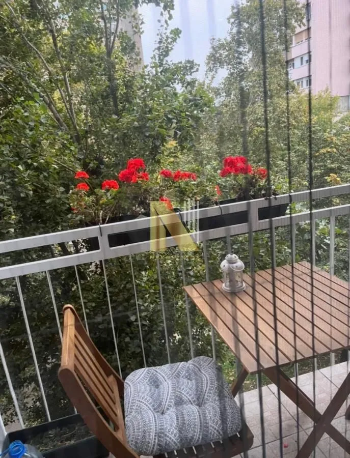 Manji namešteni balkon sa drvenim stolom, stolicama i cvećem u saksijama.