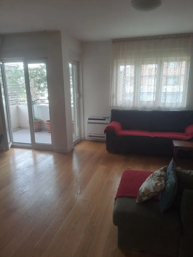 Dnevna soba sa parketom, namještajem i izlazom na balkon.