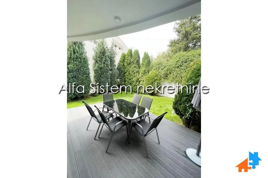 Natkrivena terasa sa stolom i stolicama i pogledom na zeleno dvorište.