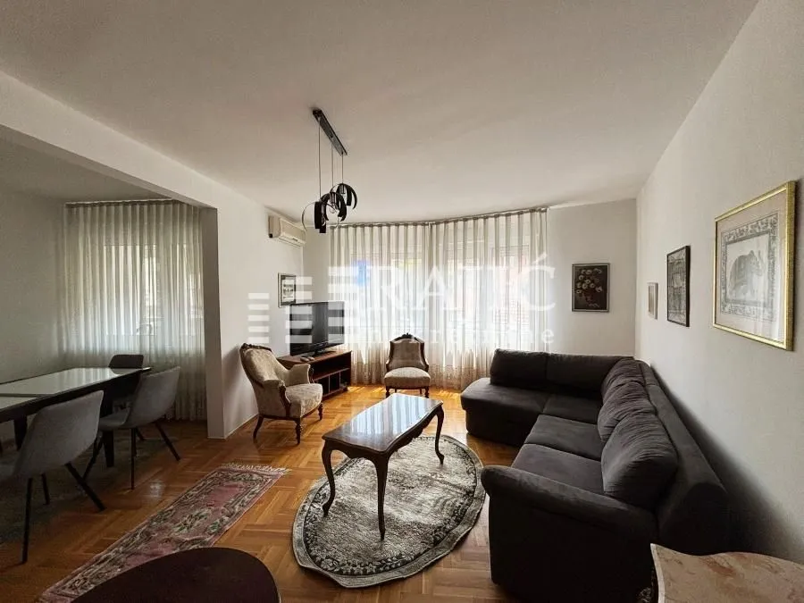 Spacious living room with a sofa set, dining table, and parquet flooring.