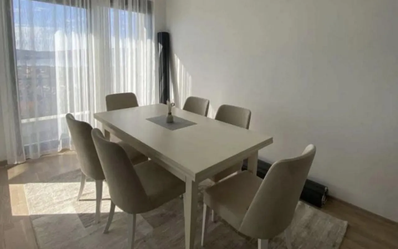 Trpezarija sa stolom i stolicama pored velikog prozora.