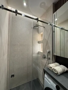 Modern bathroom with a walk-in shower and a built-in washing machine. - image 10