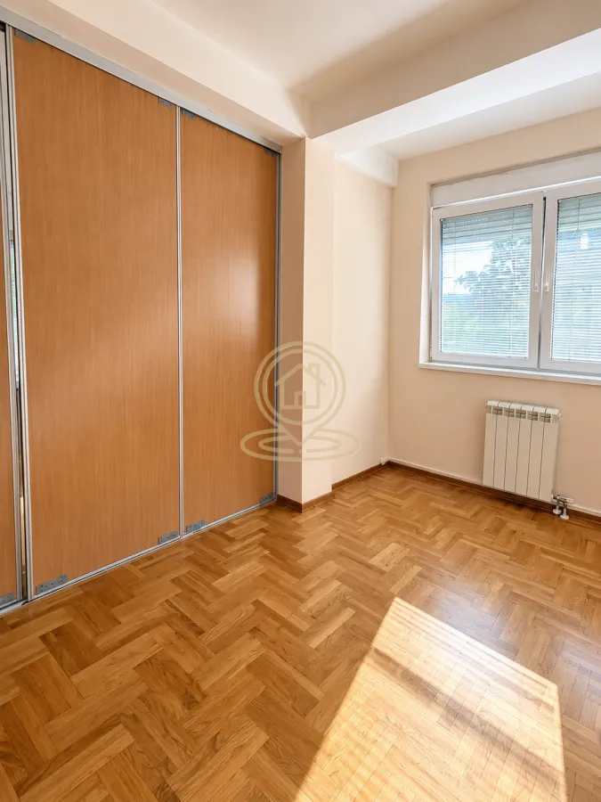 Empty room with a wooden wardrobe, parquet flooring, and a window.