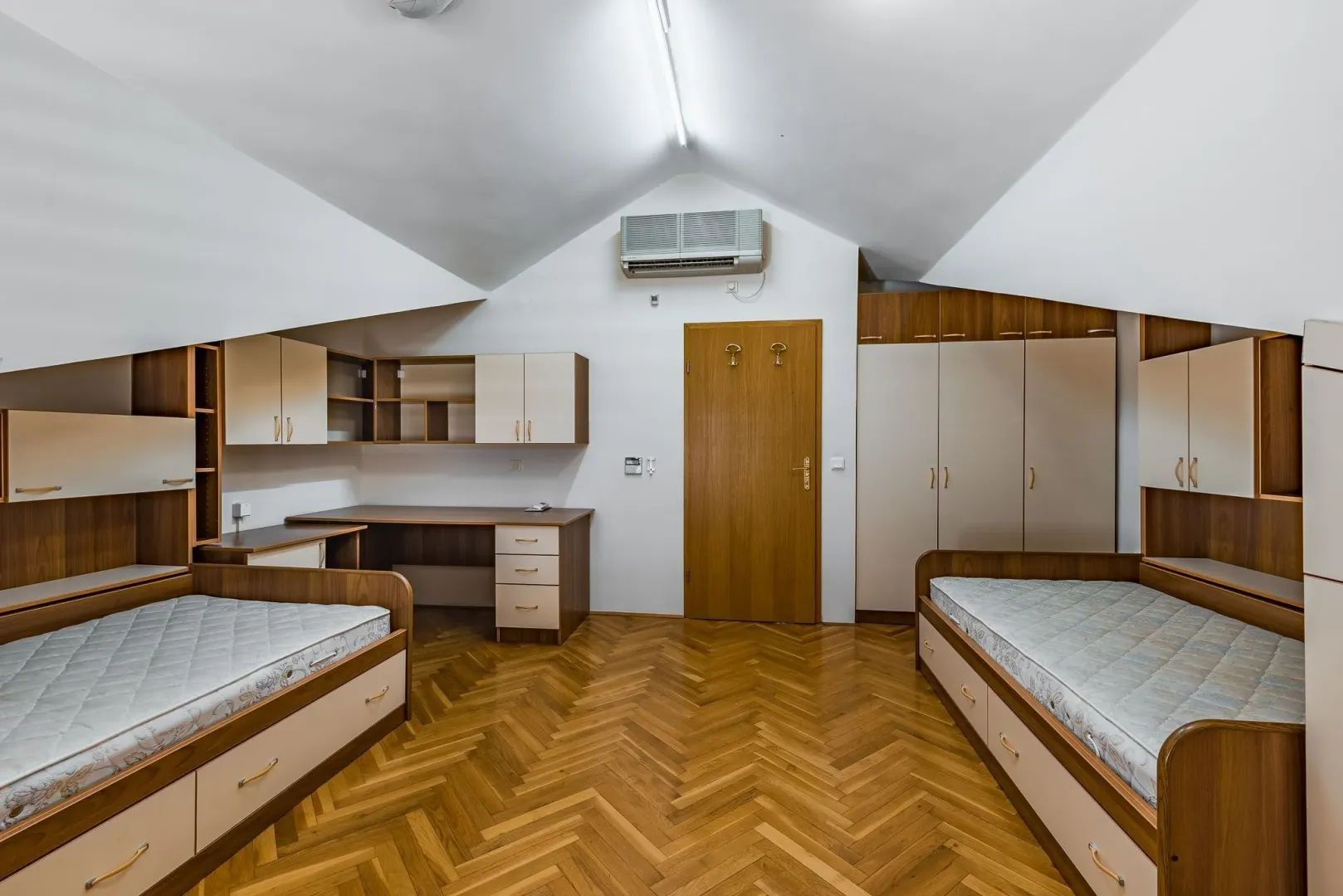 Bright attic bedroom with two single beds and wooden furniture.