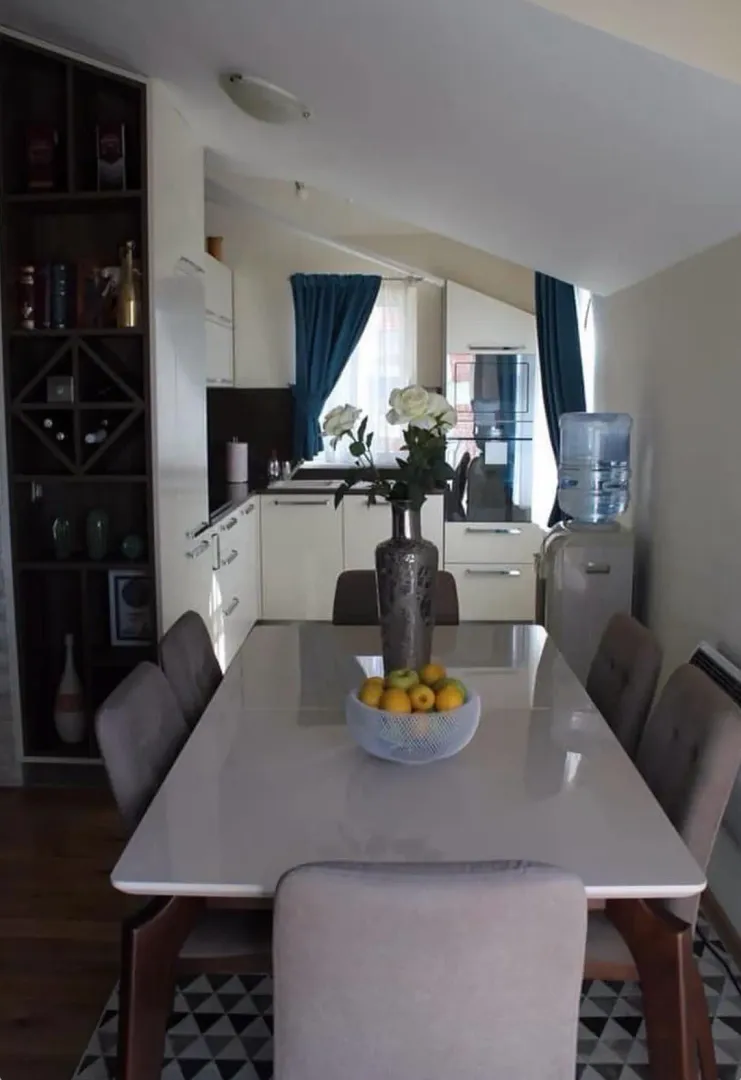 Dining area with a table, chairs, and shelving unit next to the kitchen.