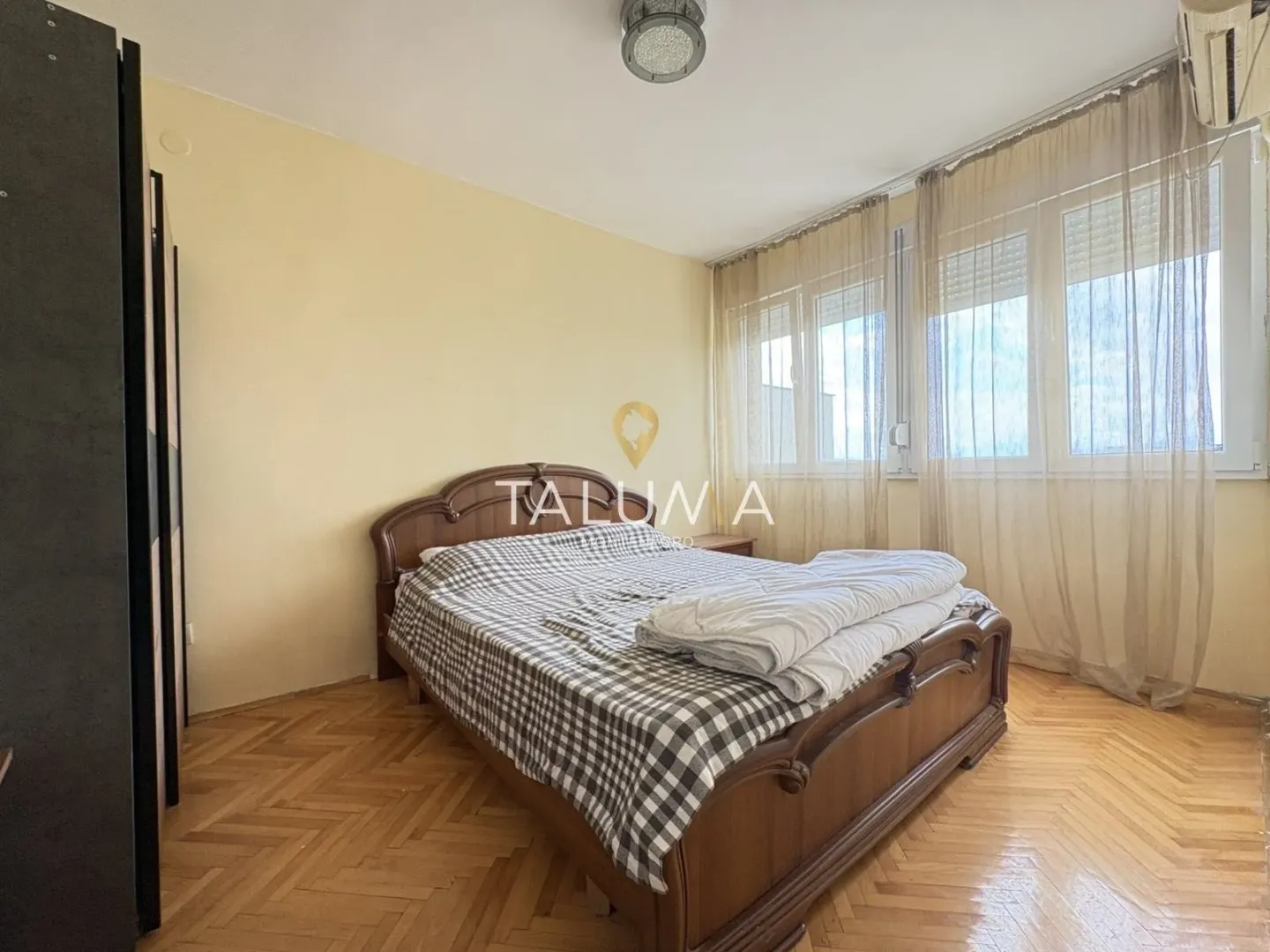 Spavaća soba sa bračnim krevetom, drvenim podom i prozorima sa zavesama.