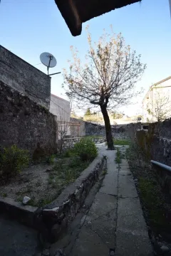 Dvorište ograđeno kamenim zidom sa betonskom stazom i drvetom. - image 8
