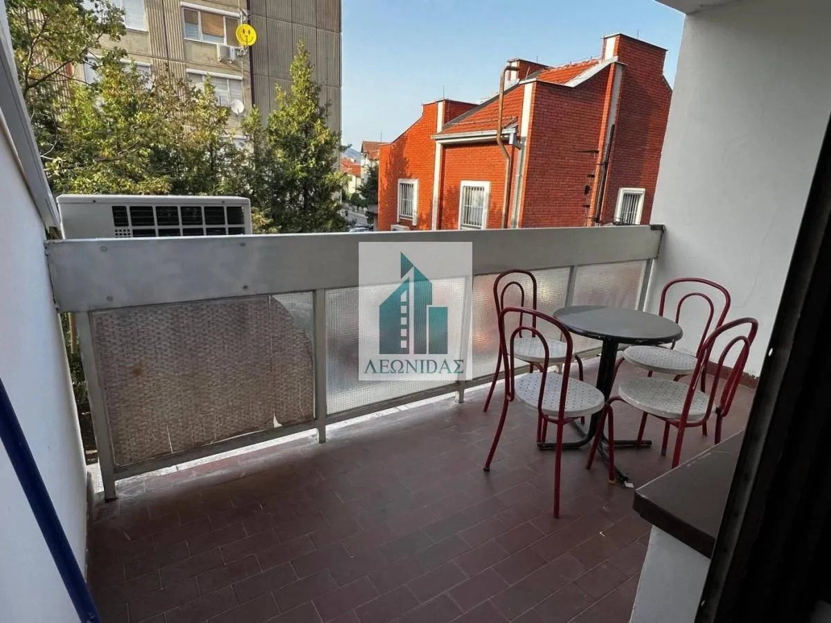 Small furnished balcony with a table and chairs and a view of surrounding buildings.