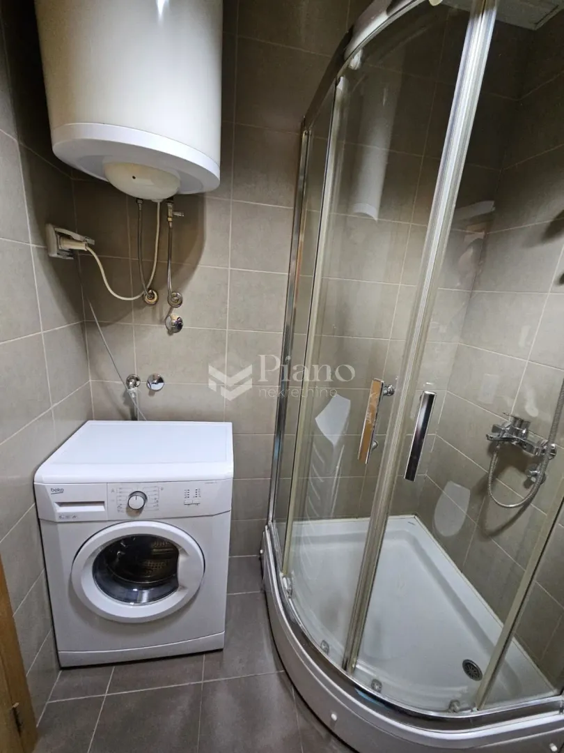 Smaller bathroom with a shower cabin, water heater, and washing machine.