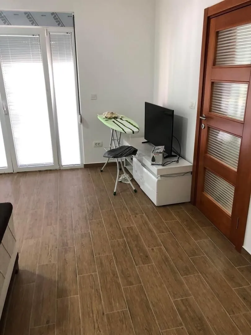 Living room with wooden flooring, a TV, and balcony doors.
