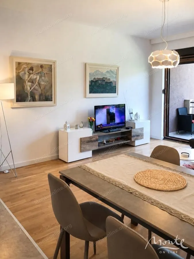 Dnevni boravak sa trpezarijskim stolom, televizorom i izlazom na terasu.