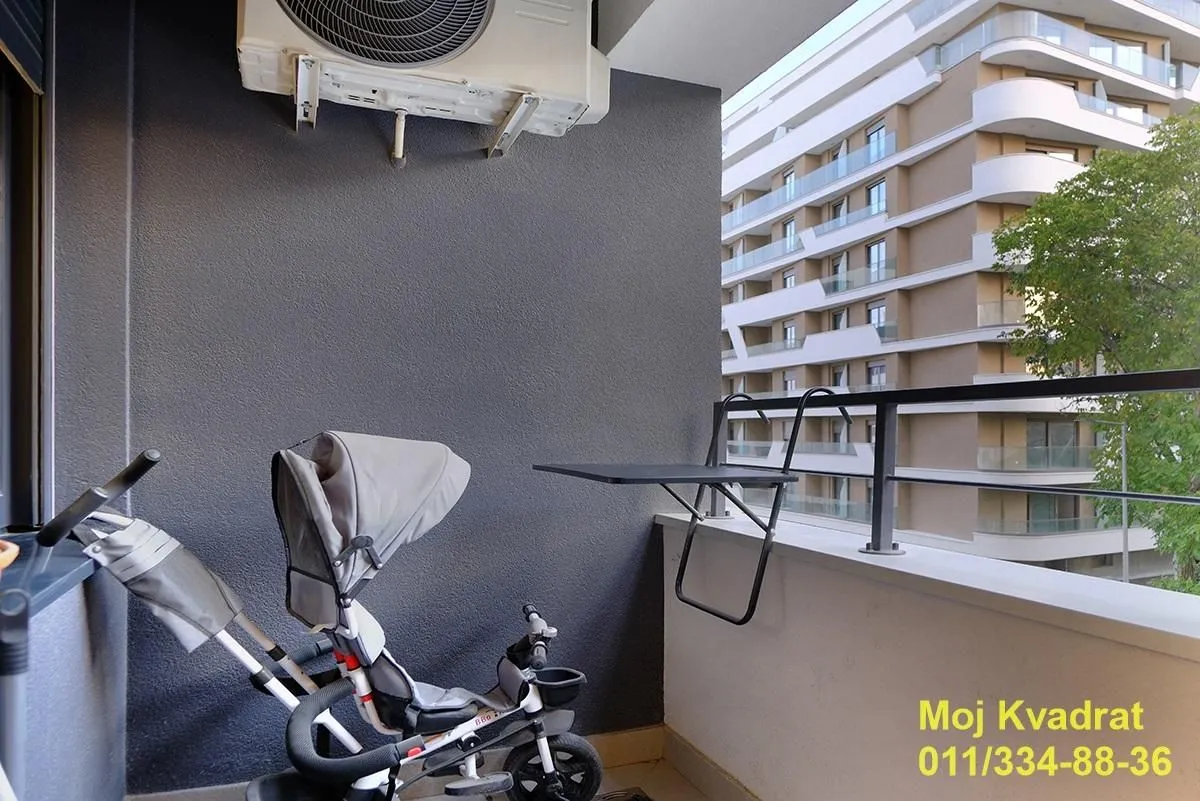 A small balcony with a child's tricycle and a view of surrounding buildings.