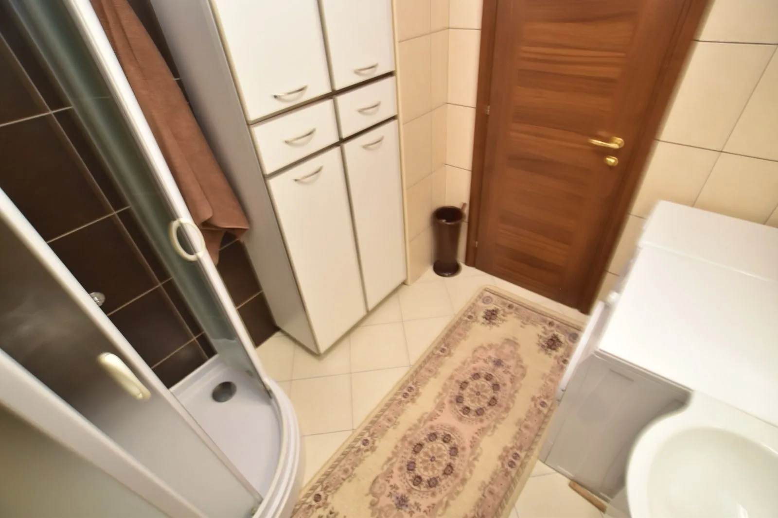 Svijetlo kupatilo sa tuš kabinom, bijelim ormarićem i veš mašinom.