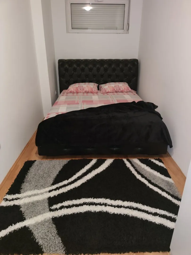 A bedroom with white walls, a double bed, and a black and white rug.