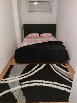 A bedroom with white walls, a double bed, and a black and white rug. - image 23