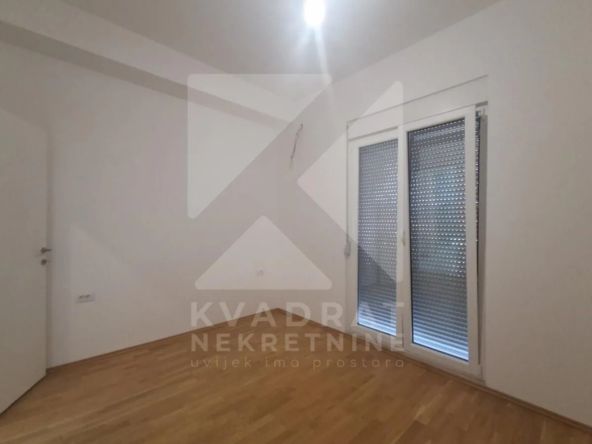 Prazna soba sa parketom i balkonskim vratima.